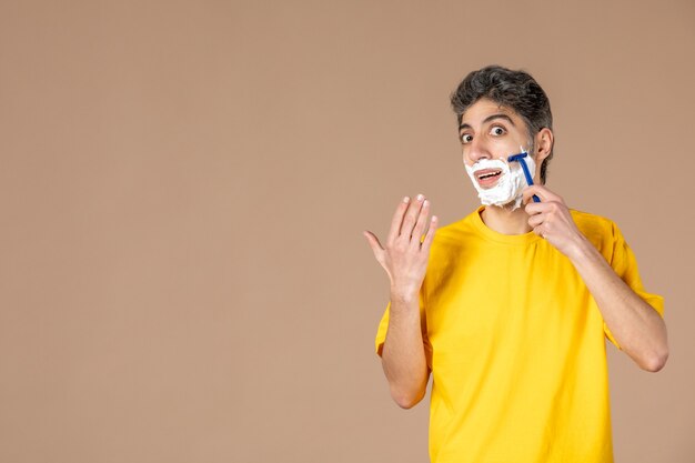 Vista frontal de los hombres jóvenes afeitando su rostro espumoso sobre fondo de color rosa