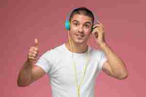 Foto gratuita vista frontal de los hombres jóvenes en camiseta blanca escuchando música a través de auriculares en el escritorio de color rosa claro