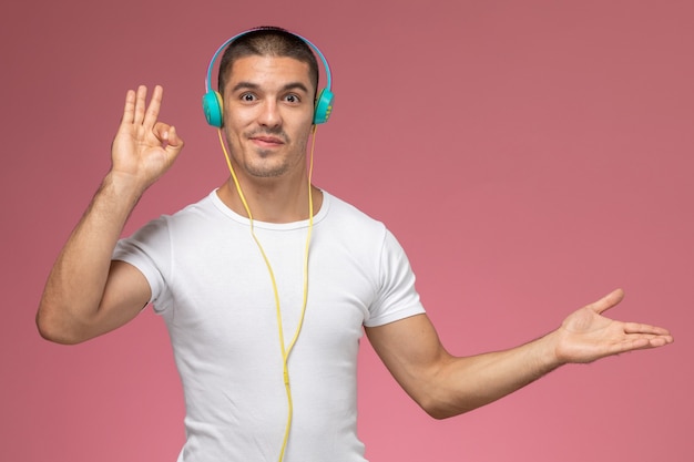 Vista frontal de los hombres jóvenes en camiseta blanca escuchando música a través de sus auriculares en el fondo rosa claro