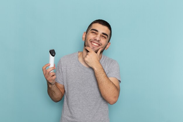 Vista frontal de los hombres jóvenes en camiseta gris con maquinilla de afeitar eléctrica sonriendo sobre espuma de pelo de barba de afeitado masculino azul hielo