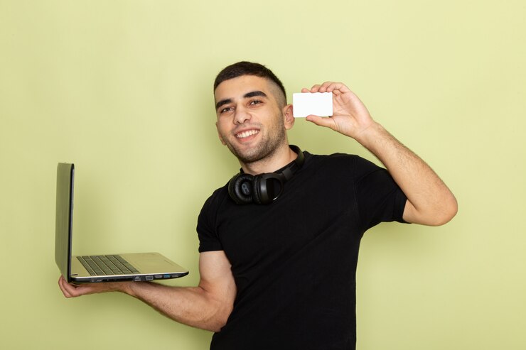 Foto gratuito vista frontal de los hombres jóvenes en camiseta negra sonriendo y usando la computadora portátil que muestra la tarjeta blanca en verde