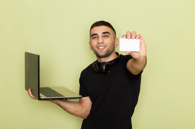 Vista frontal de los hombres jóvenes en camiseta negra sonriendo y usando la computadora portátil que muestra la tarjeta blanca en verde