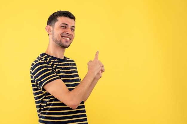 Vista frontal de los hombres jóvenes en camiseta a rayas en blanco y negro apuntando hacia atrás sobre fondo amarillo aislado