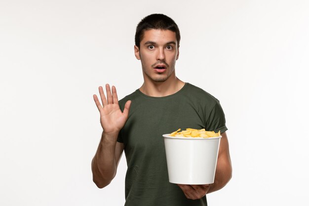 Vista frontal de los hombres jóvenes en camiseta verde con patatas cips viendo la película en el escritorio blanco película persona masculina cine de película solitario