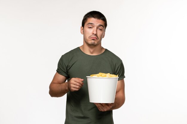 Vista frontal de los hombres jóvenes en camiseta verde con patatas cips viendo la película en la pared blanca película persona masculina cine película solitaria