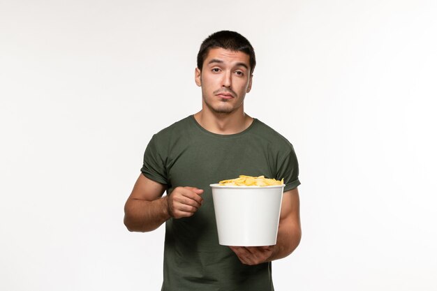 Vista frontal de los hombres jóvenes en camiseta verde con patatas cips viendo la película en la pared blanca película persona masculina cine película solitaria