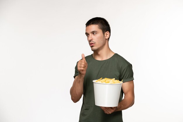 Vista frontal de los hombres jóvenes en camiseta verde sosteniendo la canasta con cips en la pared blanca película persona masculina cine de película solitario