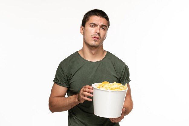 Vista frontal de los hombres jóvenes en camiseta verde sosteniendo la cesta con patatas cips en la pared blanca película de cine solitario disfrute de la película