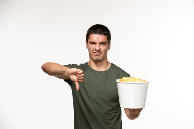 Vista frontal de los hombres jóvenes en camiseta verde sosteniendo cips de patata mostrando signo diferente en la pared blanca película solitaria película persona de cine