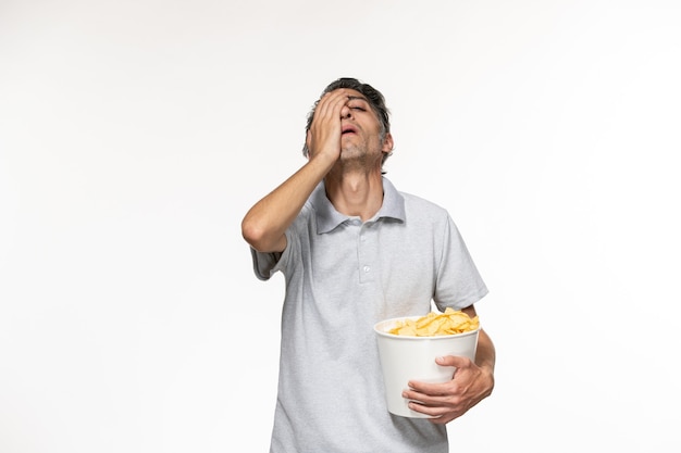 Vista frontal de los hombres jóvenes comiendo papas fritas mientras ve la película en el escritorio blanco