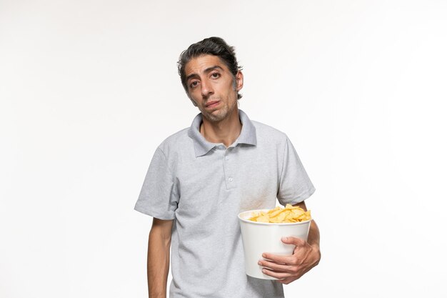 Vista frontal de los hombres jóvenes comiendo papas fritas mientras ve la película en la superficie blanca