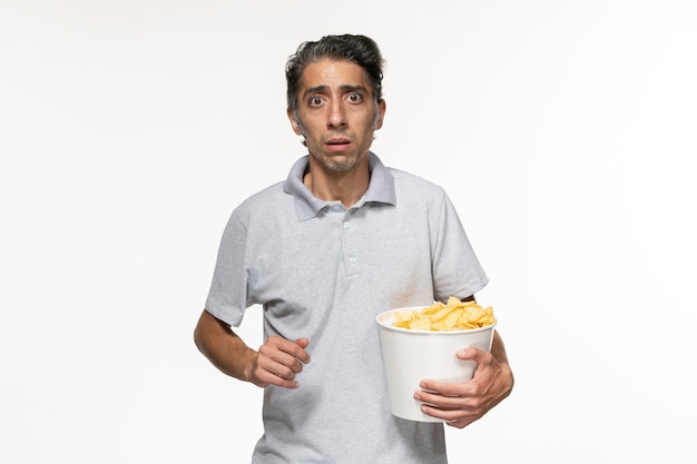 Vista frontal de los hombres jóvenes comiendo papas fritas viendo la película en la superficie blanca