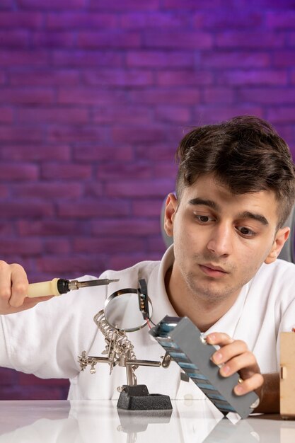 Vista frontal de los hombres jóvenes detrás del escritorio tratando de arreglar un pequeño diseño en la pared púrpura