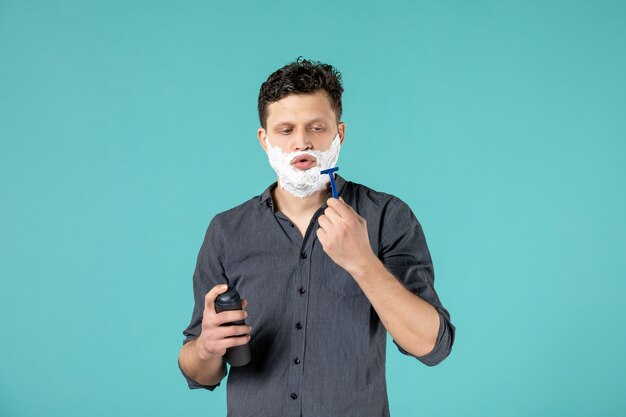 Vista frontal de los hombres jóvenes con espuma en la cara preparándose para afeitarse sobre fondo azul.