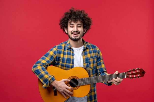 Vista frontal de los hombres jóvenes con guitarra en la pared roja, concierto en vivo, música, aplauso, banda de color, músico