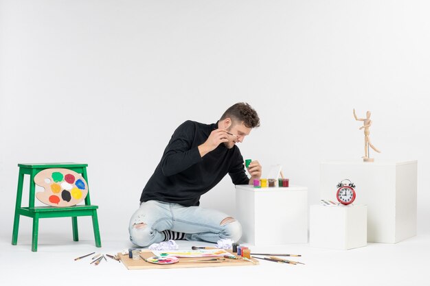 Vista frontal de los hombres jóvenes que trabajan con pinturas en la pared blanca pintura arte color artista pintura fotos imagen dibujar
