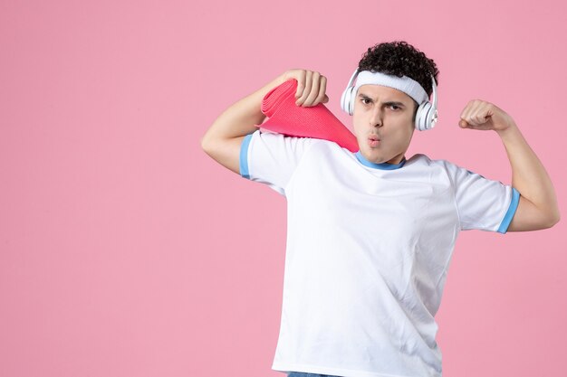 Vista frontal de los hombres jóvenes en ropa deportiva con estera de yoga y auriculares en la pared rosa