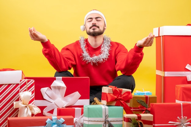 Vista frontal de los hombres jóvenes sentados alrededor de regalos y meditando sobre fondo amarillo