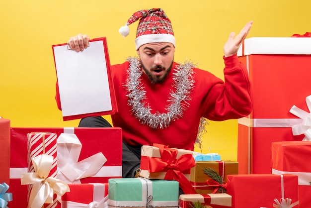 Vista frontal de los hombres jóvenes sentados alrededor de los regalos de Navidad con una nota sobre fondo amarillo