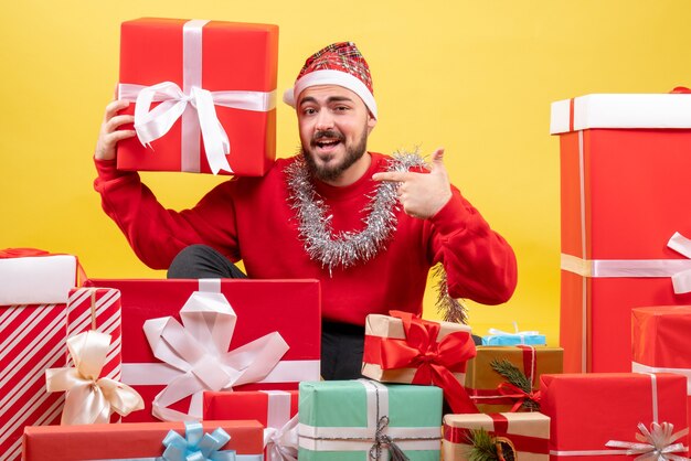 Vista frontal de los hombres jóvenes sentados alrededor de los regalos de Navidad sobre fondo amarillo