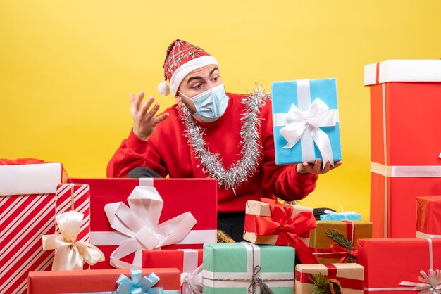 Vista frontal de los hombres jóvenes sentados alrededor de los regalos de Navidad sobre fondo amarillo