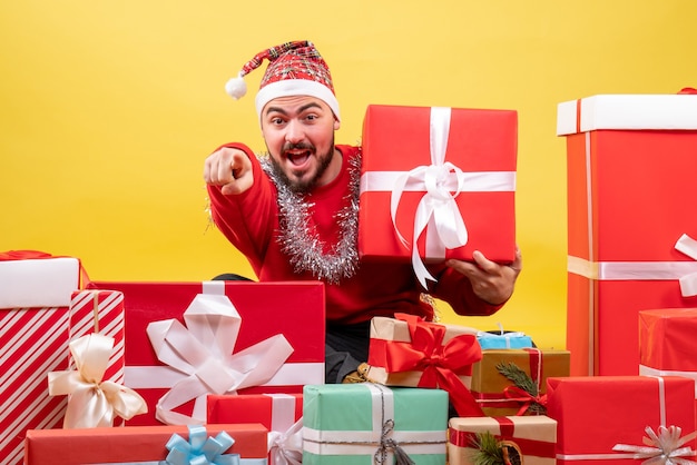 Vista frontal de los hombres jóvenes sentados alrededor de los regalos de navidad sobre fondo amarillo