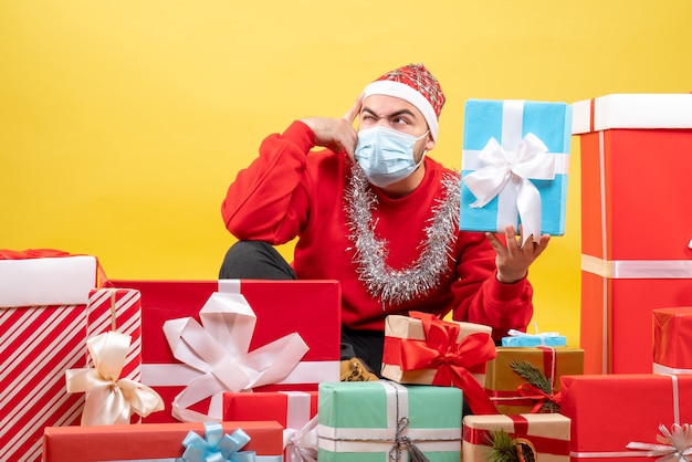 Vista frontal de los hombres jóvenes sentados alrededor de los regalos de Navidad sobre fondo amarillo