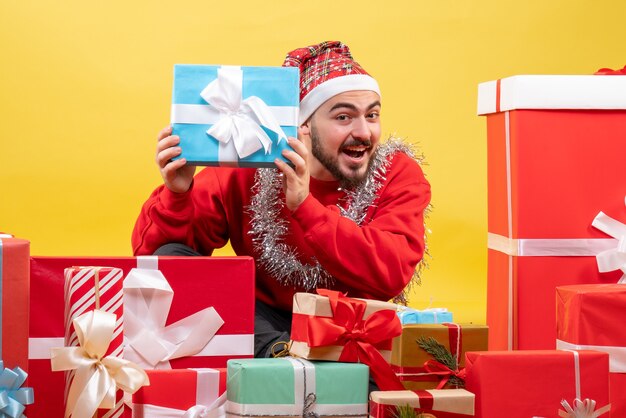 Vista frontal de los hombres jóvenes sentados alrededor de los regalos de Navidad sobre fondo amarillo