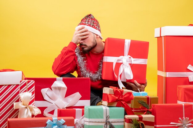 Vista frontal de los hombres jóvenes sentados alrededor de los regalos de Navidad sobre fondo amarillo