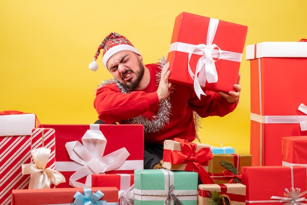 Vista frontal de los hombres jóvenes sentados alrededor de los regalos de Navidad sobre fondo amarillo