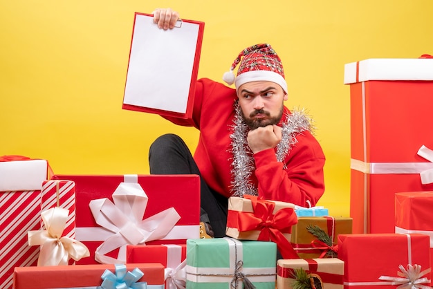 Vista frontal de los hombres jóvenes sentados alrededor de regalos con una nota sobre el escritorio amarillo