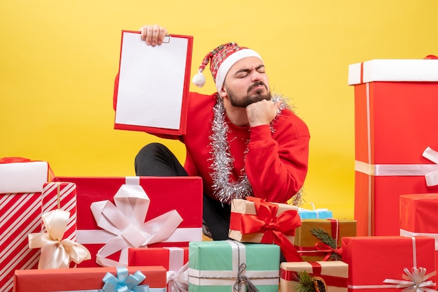 Vista frontal de los hombres jóvenes sentados alrededor de regalos con una nota sobre fondo amarillo