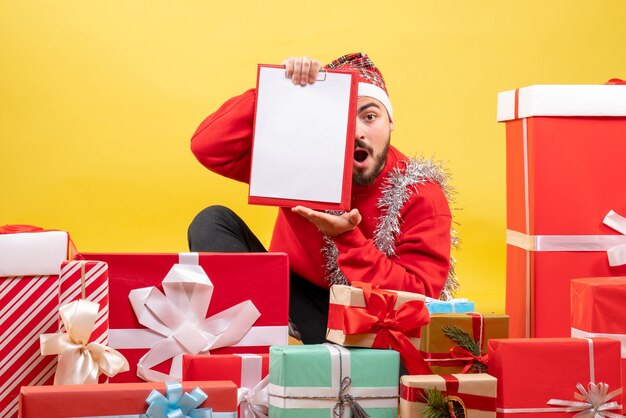 Vista frontal de los hombres jóvenes sentados alrededor de regalos con una nota sobre fondo amarillo