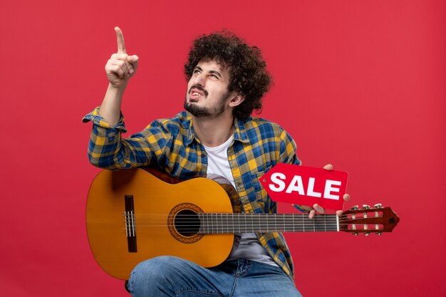 Vista frontal de los hombres jóvenes sentados con la guitarra en la pared roja, concierto, música en vivo, color, aplauso, músico, juego