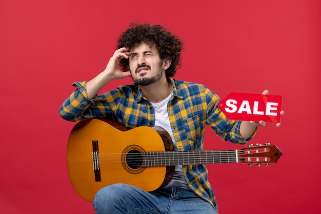 Foto gratuita vista frontal de los hombres jóvenes sentados con la guitarra en la pared roja reproducir música músico color aplauso venta en vivo