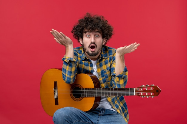 Vista frontal de los hombres jóvenes sentados con la guitarra en la pared roja tocar música de concierto músico de color aplausos banda en vivo