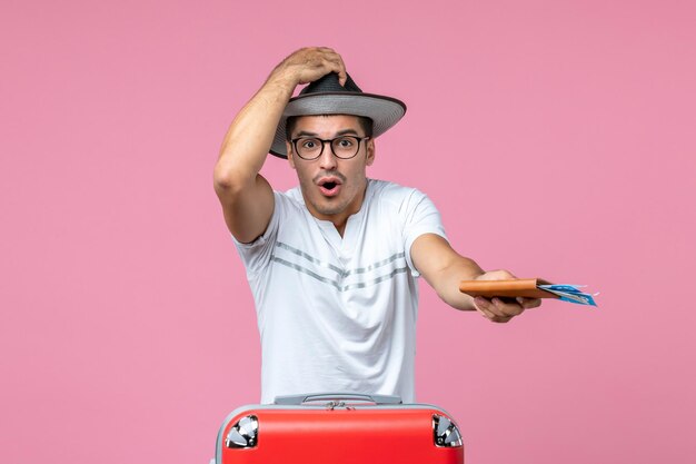 Vista frontal de los hombres jóvenes con sombrero y sosteniendo boletos de avión en la pared rosada viaje en avión masculino foto color viaje vacaciones