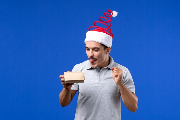 Vista frontal de los hombres jóvenes sosteniendo el paquete de alimentos en la pared azul trabajo masculino ser humano