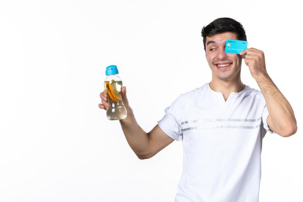 Vista frontal de los hombres jóvenes sosteniendo una tarjeta de crédito azul y una botella de limonada sobre fondo blanco jugo dinero fruta bebida refresco helado fresco