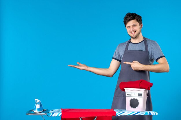 Vista frontal de los hombres jóvenes con tabla de planchar sobre el fondo azul lavandería plancha color hombre lavadora quehaceres domésticos limpieza