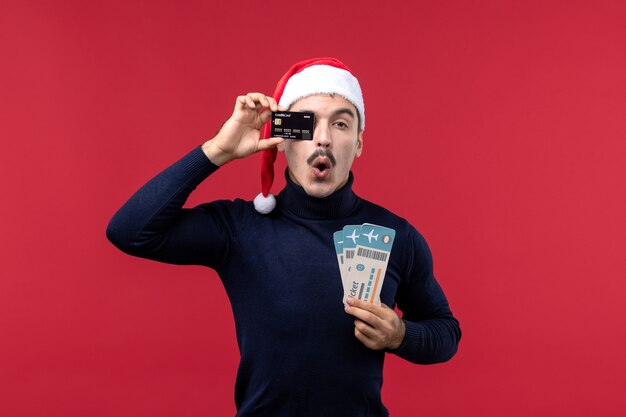 Vista frontal de los hombres jóvenes con tarjeta bancaria y billetes sobre fondo rojo.