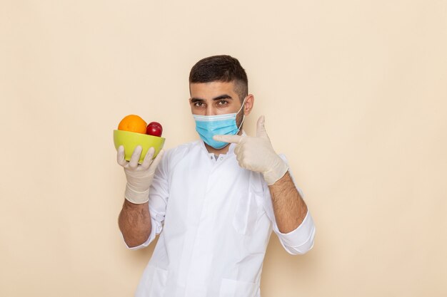 Vista frontal de los hombres jóvenes en traje blanco con máscara y guantes con plato con frutas