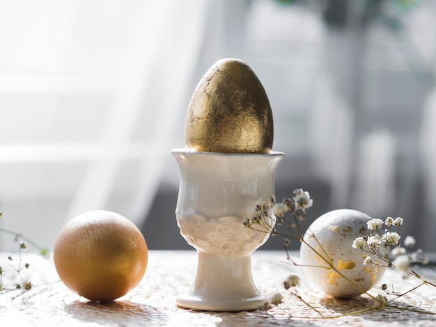 Vista frontal del huevo de pascua dorado en soporte con gypsophila