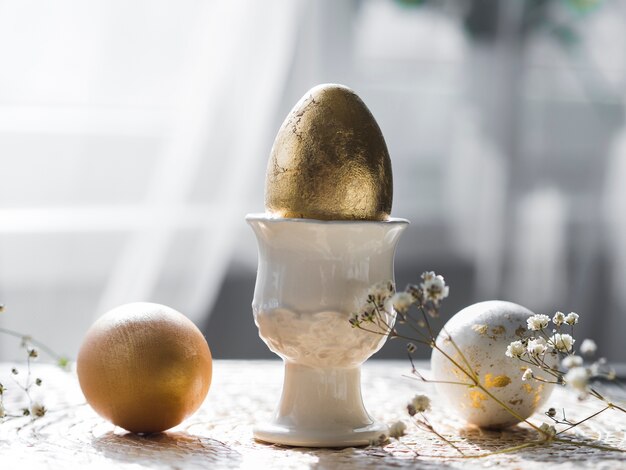 Vista frontal del huevo de pascua dorado en soporte con gypsophila