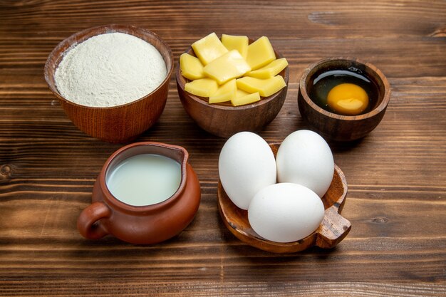 Vista frontal de huevos crudos enteros con harina de queso y leche en la mesa de madera marrón producto masa de huevo pastelería