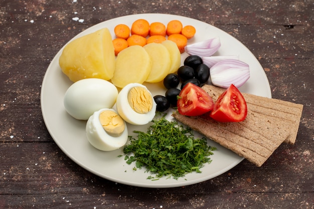 Vista frontal de los huevos duros con aceitunas verdes, ajo y tomates dentro de la placa en el fondo marrón desayuno comida vegetal