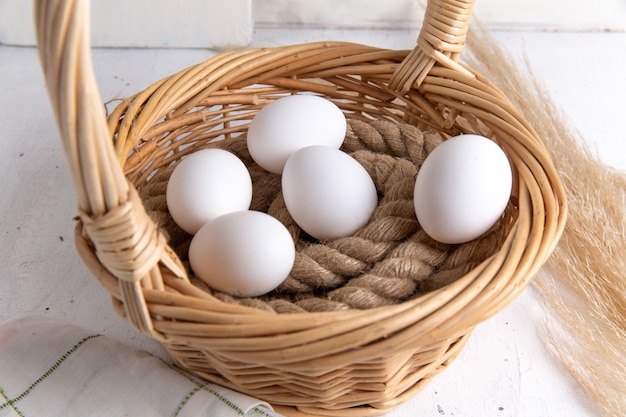 Vista frontal de huevos enteros blancos dentro de la cesta sobre el fondo blanco.