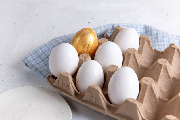 Vista frontal de huevos enteros blancos con uno dorado sobre fondo blanco.