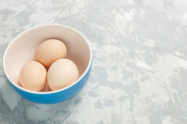 Vista frontal de huevos enteros crudos dentro de un plato pequeño en un escritorio blanco claro