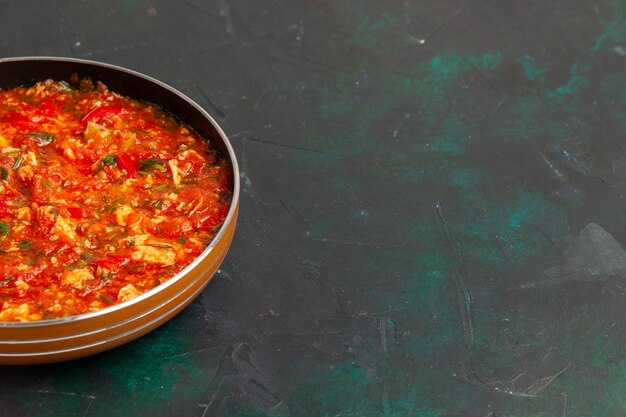 Vista frontal de huevos revueltos con tomates y verduras dentro de la sartén sobre la superficie verde oscuro